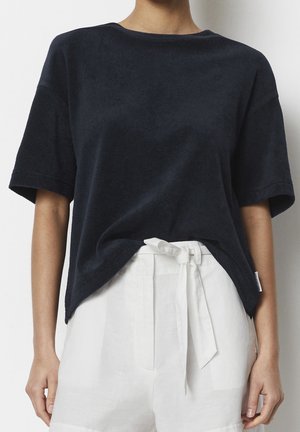 Granatowy T-shirt z krótkim rękawem wykonany z miękkiej, teksturowanej tkaniny. Okrągły dekolt, lekko zaokrąglony dół, zestawiony z białymi lnianymi spodniami wiązanymi w talii.