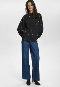 Schwarze Knopf-bluse mit floralem Stickerei; kombiniert mit weiten denimbuxen und schwarzen Absatzstiefeln. Glatter Stoff, lockere Passform.