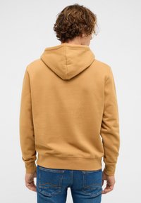 Brązowa bawełniana bluza z kapturem ze ściągaczem, plisowanymi mankietami i pasem, noszona na niebieskich dżinsach. Tkanina ma gładką, miękką fakturę.