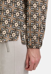 Bluse mit Muster in Schwarz, Weiß und Pfirsich, die ein florales Design aufweist, mit elastischen Bündchen und einem leichten Seitenschlitz am Saum.