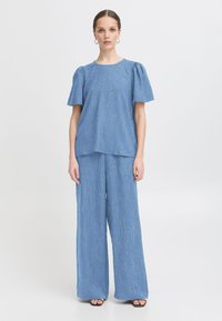 Bluză texturată albastră cu mâneci bufante, asortată cu pantaloni evazați. Țesătura are dungi verticale subtile și o croială lejeră.