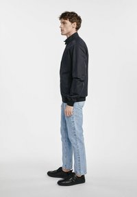 Granatowa kurtka bomberka z zamkiem z przodu, ściągaczem przy kołnierzu i mankietach, w połączeniu z jasnoniebieskimi jeansami o prostym kroju i czarnymi trampkami.