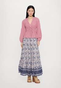 Gestreifte Bluse in Rot und Weiß mit Raffung und langen Ärmeln, kombiniert mit einem floralen, gestuften Maxirock mit blauen Akzenten. Chunky Absatzsandalen.
