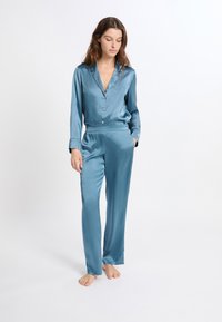 Satijnen slaapset in teal. Langsleeve shirt met knopen en kraag, gecombineerd met broek met elastische taille. Soepele, glanzende textuur.