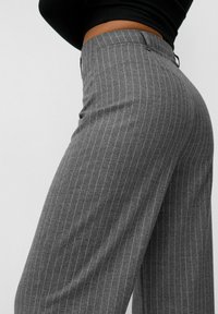 Pantalons gris à rayures avec une coupe décontractée, présentant une texture lisse et un design classique. La taille comprend des passants de ceinture et des poches arrière.
