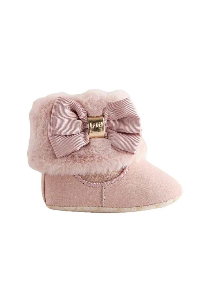 Chausson de bébé rose doux avec bord en fausse fourrure et grand nœud texturé avec une petite étiquette métallique dorée au centre.