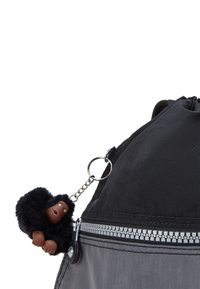 Sort nylon rygsæk med en sølv lynlås og et rundt lynlåstræk, udsmykket med en sort abe nøglering lavet af kunstpels og plastik.