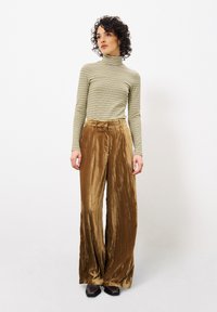 Gestreepte lange mouwen top in groen en gebroken wit, gecombineerd met hoge taille, wijde, bruine fluwelen broek; gladde textuur en subtiele glans.