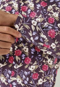 Bloemenoverhemd met knopen in donkerpaars, met roze, witte en groene bloempatronen, met een zachte textuur en knoopmanchetten.
