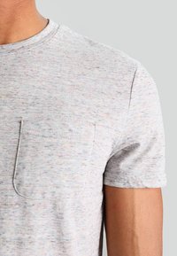 Camiseta de manga corta gris claro con textura moteada y bolsillo en el lado izquierdo del pecho. Cuello redondo; material de mezcla de algodón.