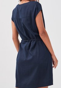 Abito in lino blu navy con maniche corte, vestibilità rilassata, vita cinchata con un laccio intrecciato e un sottile dettaglio di cucitura sul dietro.