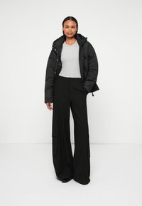 Svart puffjacka med huva, grå åtsittande skjorta och vida svarta byxor med cargofickor. Slät tyg och avslappnad passform genom hela outfiten.