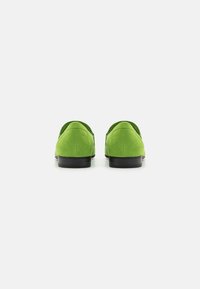 Mocasines de ante verde con una textura suave, tacones bajos negros y respaldos redondeados, que exhiben un diseño simple y clásico.