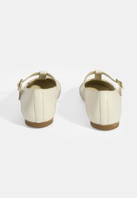 Cremfarbene Ballerinas aus Leder mit runder Zehenpartie, Knöchelriemen und kleinen Schnallendetails. Glatte Textur und niedriger, brauner Gummihügel.