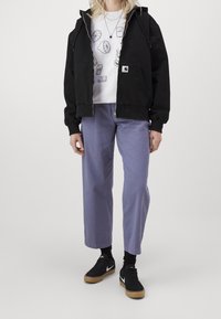 Black zip-up hooded jacket, white graphic sweatshirt, light purple wide-leg pants, and black sneakers with white accents.