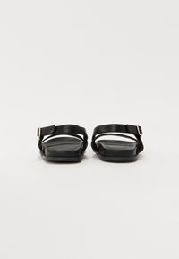 Sandalias negras con suela plana, con correas entrelazadas y una hebilla lateral. Textura suave y diseño minimalista.