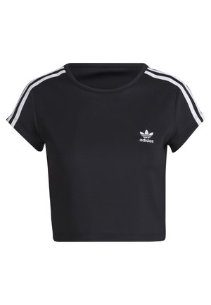 Kobieta w czarnym krótkim t-shircie Adidas z białymi paskami na rękawach i czarnych skórzanych spodniach ze sznurkiem na białym tle.