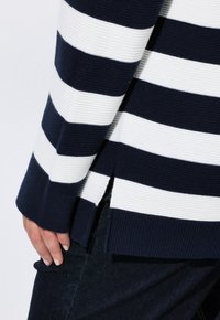 Marinblå och vitrandig tröja med ribbad textur, sidoremmar och långa ärmar. Materialet verkar vara stickat.