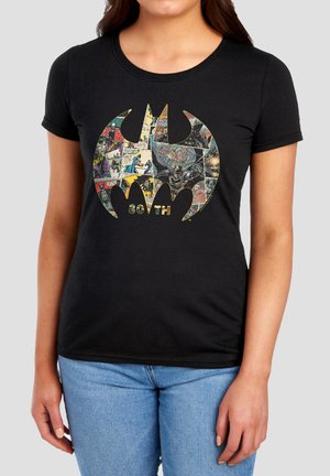 Frau, die ein schwarzes T-Shirt mit einem großen Batman-Logo trägt, das mit Comicstrip-Bildern gefüllt ist, und darunter steht der Text "80TH".