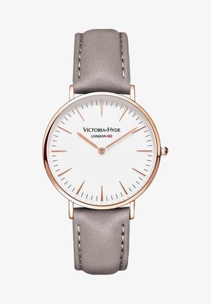 Quadrante bianco rotondo con accenti in oro rosa e indicatori delle ore sottili, montato su un cinturino in pelle grigia chiara con cuciture bianche.