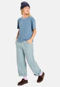 Kék pamut póló zöld kockás nadrággal párosítva. A modell sötétkék sapkát és barna, könnyen felhúzható cipőket visel rózsaszín zoknival.