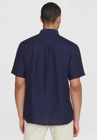 Kurzarmhemd aus dunkelblauem Leinen mit einem Umlegekragen, Rückenfalte und geradem Saum. Weiche Textur mit lockerer Passform.