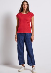 Červený top s krátkým rukávem a výstřihem do V, v páru s volnými modrými džínami. Bílé tenisky doplňují ležérní vzhled.