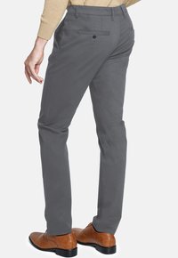 Pantalones grises con un diseño de pierna recta, que presentan bolsillos traseros con cierres de botón y una suave tela de algodón. Zapatos de vestir marrones visibles.