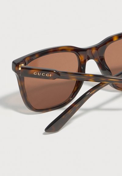 Lunettes de soleil à monture écaille avec verres marron, ornées de l'inscription "GUCCI" gravée en or sur la branche.