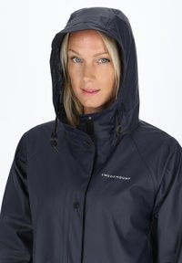 Granatowa wodoodporna kurtka z kapturem, z przodem zapinanym na napy i akcentami z możliwością regulacji. Posiada logo "SWEDEMOUNT" na klatce piersiowej.
