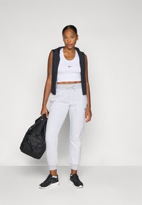 Conjunto deportivo que incluye un crop top blanco ajustado, pantalones de chándal grises y una sudadera negra, combinados con zapatillas negras y una bolsa de deporte negra.