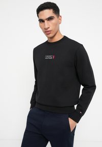 Μαύρος φούτερ με στρογγυλή λαιμόκοψη και ραμμένα μανίκια, με κόκκινο και λευκό λογότυπο "TOMMY HILFIGER" στο στήθος. Απαλή βαμβακερή ύφανση.