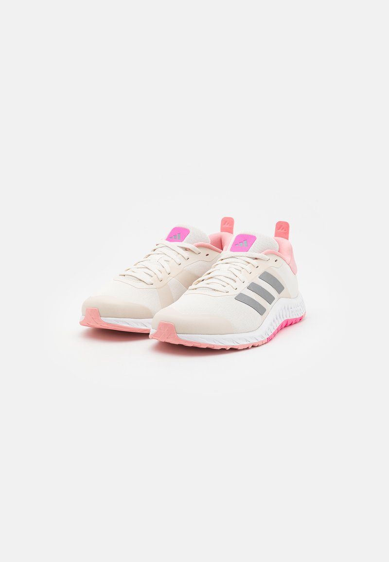 Zapatillas deportivas beige con parte superior de malla, acentos en rosa, rayas grises y una suela texturizada. Incluyen un cuello acolchado y una suela de contraste.
