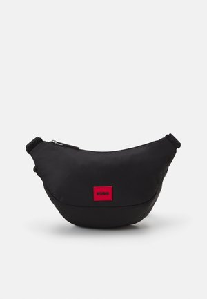 Schwarze Nylon-Tasche mit geschwungener Form, versehen mit einem roten rechteckigen Logo-Patch und verstellbarem Riemen, Reißverschluss und glatter Textur.