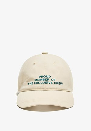 Bežová bavlnená šiltovka s vyšitým textom v odtieni teal: "HRDÝ ČLEN EXKLUZÍVNEJ POSÁDKY." Klasický zakrivený šilt.