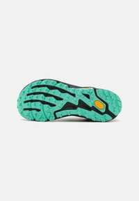 Fekete sportcipő talpa, türkiz gumitalppal, háromszögletű mintázattal a tapadás érdekében, valamint egy sárga Vibram logó részlettel.