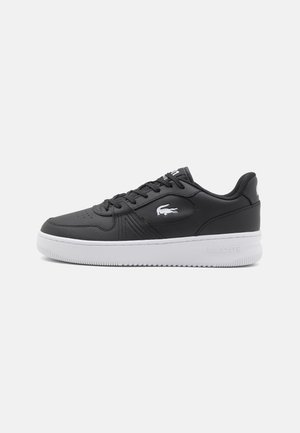 Baskets basses noires à semelle blanche, design à lacets et logo crocodile blanc sur le côté, mettant en avant la marque Lacoste.