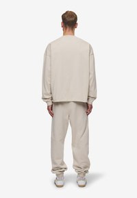 Sudadera de algodón beige con hombros caídos, combinada con pantalones de chándal de corte holgado a juego. Presenta puños acanalados y un diseño casual.