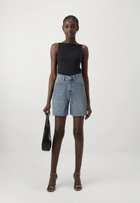 Top negro sin mangas, pantalones cortos de mezclilla azul claro de talle alto con dobladillo deshilachado, combinados con sandalias de tacón alto con tiras y un bolso negro.