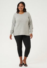 Light gray knit sweater with long sleeves, round neckline, and side slits, paired with black slim-fit pants and block-heeled black sandals.