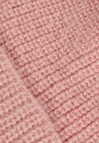 Tessuto lavorato a maglia in un morbido rosa chiaro, con un motivo testurizzato e punti in rilievo, che mostra una leggera lucentezza e un aspetto accogliente.