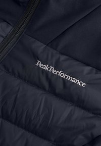 Námořnická prošívaná bunda s hladkým povrchem, zapínáním na zip a vyšitým logem "PeakPerformance" na hrudi.