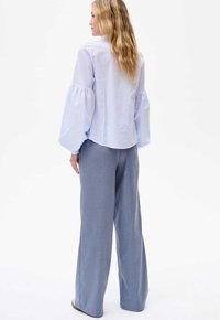 Lichtblauwe gestreepte blouse met pofmouwen, gecombineerd met losse grijze broeken. Soepele texturen en een ontspannen pasvorm.