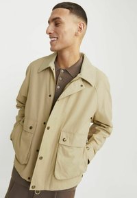 Beige jakke med en kordfløjlskrave, knaplukning foran, to frontlommer og en afslappet pasform. Materialet virker glat og let.