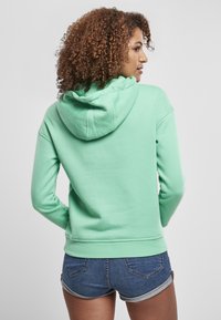 Felpa verde menta con coulisse, caratterizzata da orlo e polsini a coste, abbinata a pantaloni corti di jeans. Tessuto morbido, design casual.