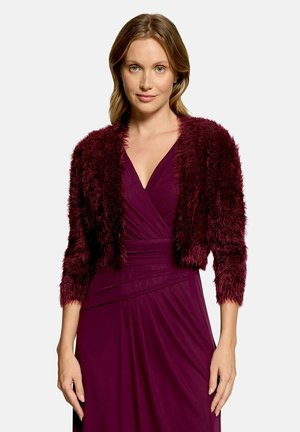 Woman with light brown hair wearing a dark purple wrap dress and a matching fluffy cropped cardigan with three-quarter sleeves.