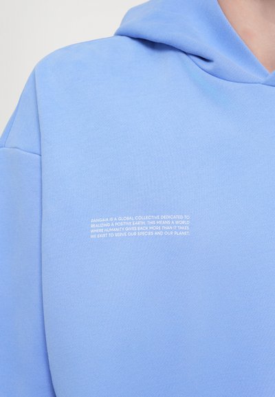 Lyseblå hættetrøje lavet af blødt materiale, med en frontknap lomme og hvid trykt tekst på siden. Enkel og afslappet design.
