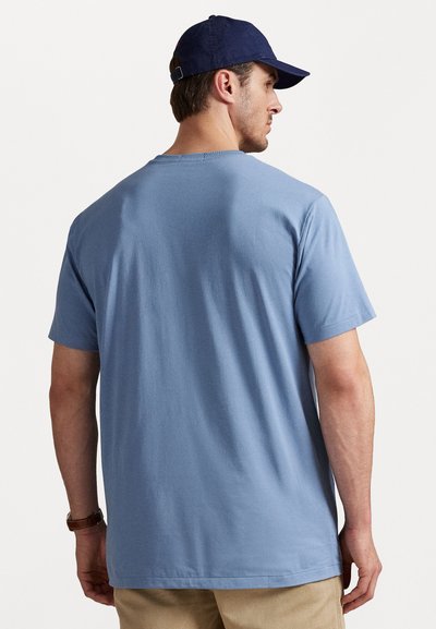 Tricou din bumbac de culoare albastru deschis, cu o croială lejeră, mâneci scurte și guler rotund, văzut din spate. Design simplu, fără modele sau grafice.