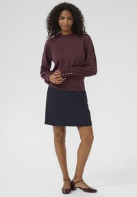Burgundy long-sleeve sweater with button accents at cuffs, paired with a fitted navy skirt and glossy burgundy shoes.