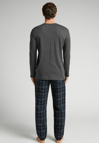 Conjunto de ropa de estar para hombres: camiseta gris de manga larga con cuello redondo, combinada con pantalones de pijama de cuadros en azul marino. Tejido suave, ajuste relajado y tonos neutros.